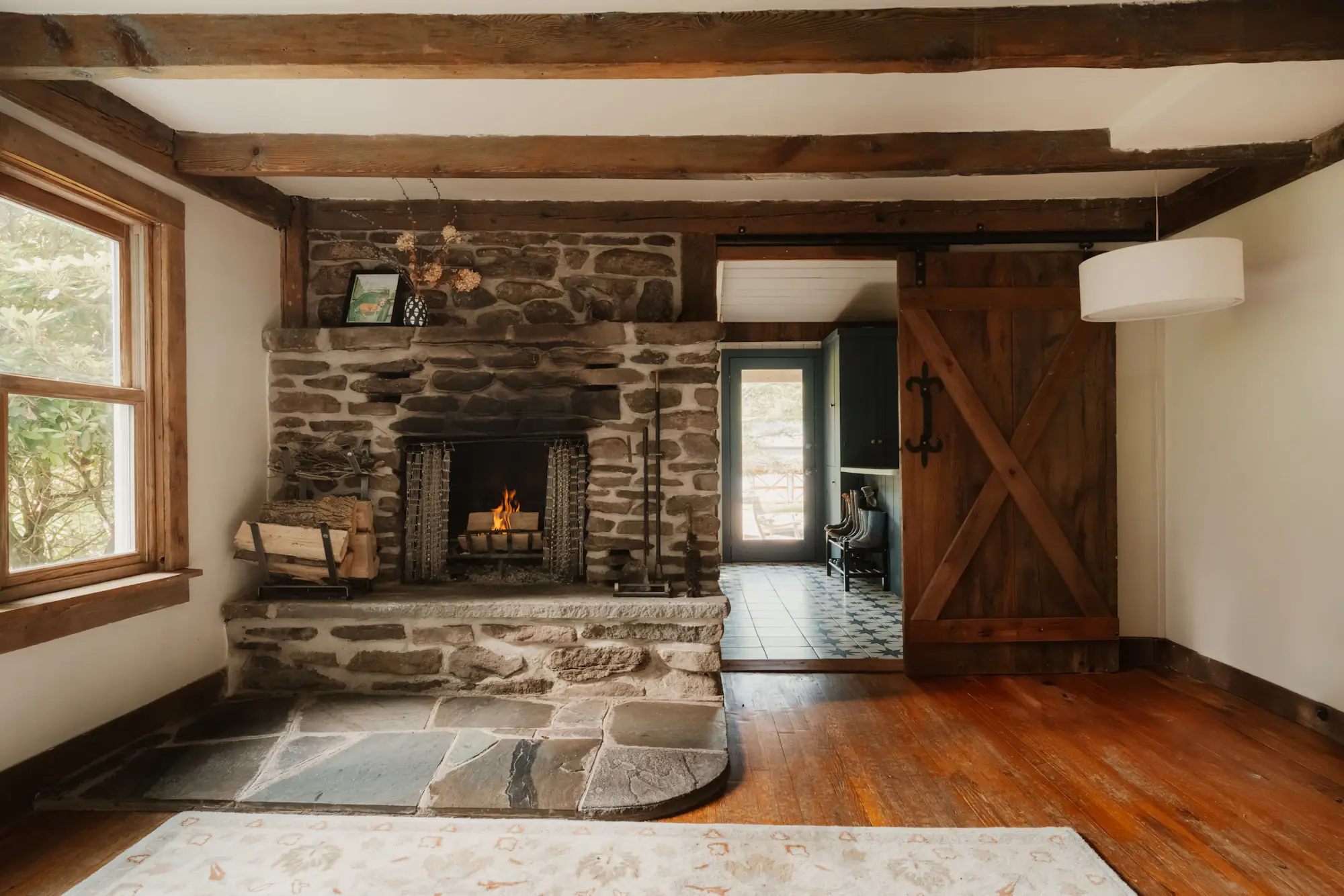 A great room with a limestone fireplace, hand-hewn beams and a sliding barn door