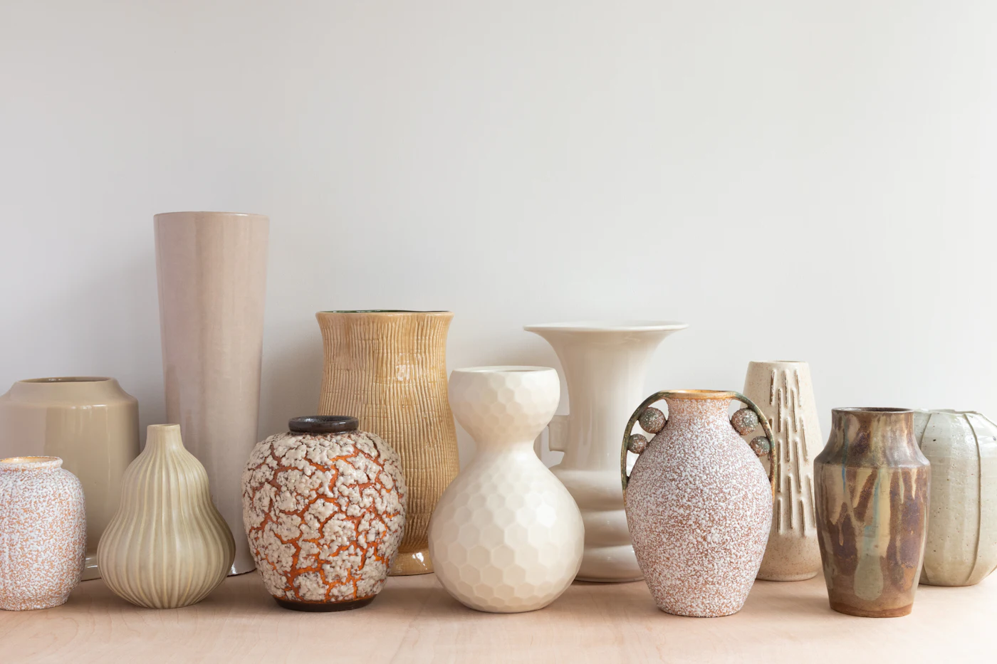 A row of hand-thrown stoneware vessels in limestone tones