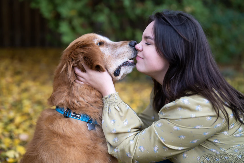 A woman kissing her golden retriever outdoors